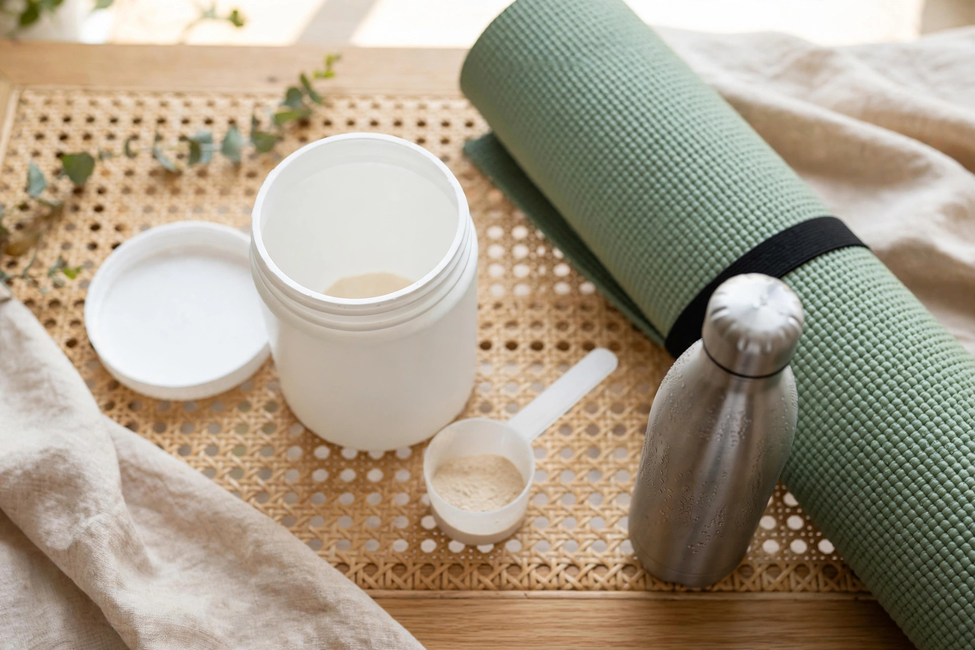 Supplement tub with a scoop of powder beside a yoga mat and water bottle